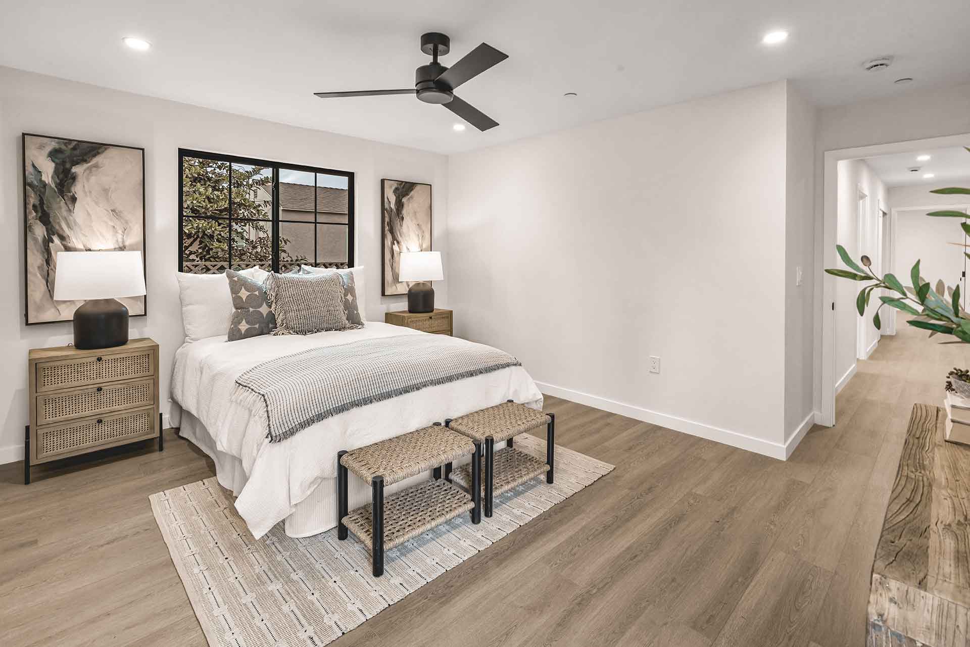 Bright ADU bedroom with wood flooring, neutral bedding, and black-framed windows.